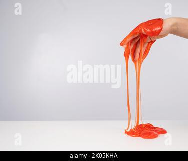 Roter Schleim, der aus der Hand einer Frau auf einem weißen Hintergrund herabfließt. Stockfoto