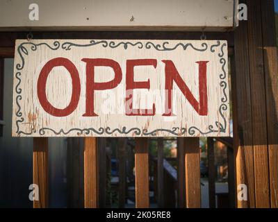 Handbemaltes Schild, das offen in roter Schrift an Bord mit rustikalem Look steht. Stockfoto