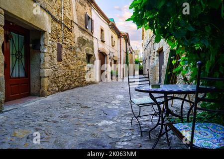 Schöne Gasse voller Steinhäuser und Eisen Tisch und Stühle zum Ausruhen, Peratallada, Girona, Spanien. Stockfoto