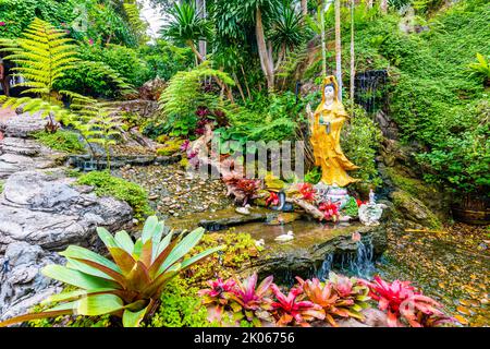 Kleiner Garten mit Wasserteich, Buddha-Statue und Blumen in der Nähe des Wat Saket-Tempels (Goldener Berg) in Bangkok, Thailand. Auf der Oberseite befindet sich ein berühmtes Religionsgebäude Stockfoto