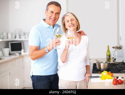 Fröhliches Seniorenpaar, das Weingläser in der Küche toaste. Porträt eines fröhlichen älteren Paares, das Weingläser in der Küche toasting. Stockfoto