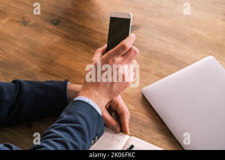 Leeres Telefon mit schwarzem Bildschirm in männlicher Hand. Arbeitsplatz zu Hause oder im Büro. Kaukasischer Mann planen und notieren Zeitplan (Urlaubsreise) auf dem Tagebuch im Büro Stockfoto