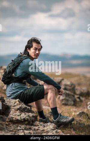 Chinesischer männlicher Trailrunner, der auf Felsen sitzt Stockfoto