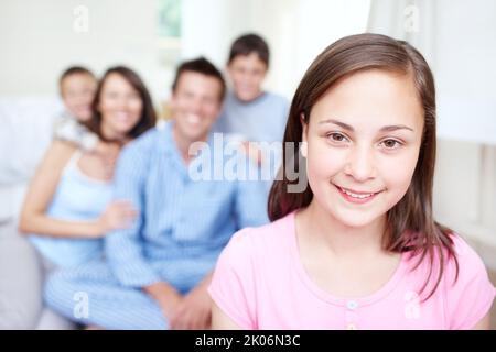 Shell hat immer ihre Familie zur Unterstützung. Porträt eines entzückenden kleinen Mädchens, das fröhlich lächelt, während ihre Familie im Hintergrund verschwommen sitzt - Stockfoto