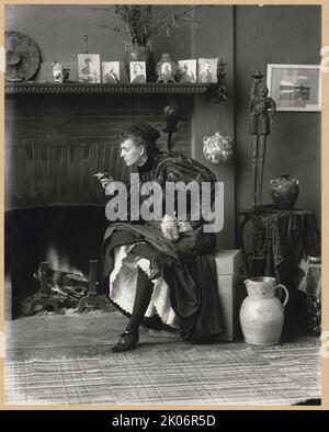 Frances Benjamin Johnston, Porträt in voller Länge, sitzt vor dem Kamin, nach links gewandt, hält Zigarette in der einen Hand und einen bierstein in der anderen, in ihrem Studio in Washington, D.C. 1896. In diesem Selbstporträt posiert die Fotografin Frances Benjamin Johnston als unabhängige „neue Frau“. Auf dem Mantelstück sind sechs Porträts von Männern zu sehen (von links nach rechts): Der Dichter Bliss Carman; A. N. Brown, wahrscheinlich Bibliothekar an der U.S. Naval Academy; Henry Guston Rogers, wahrscheinlich der Erfinder und Dramatiker Henry Gustave Rogers; der Architekt James Rush Marshall; der Smithsonian Bibliothekar Frank Phister; und L. Stockfoto