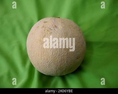 Saftig reife ganze Moschusmelone, auch bekannt als Cucumis melo in grünem Hintergrund platziert. Stockfoto