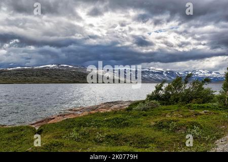 Aursjoen-Stausee, Aursjoen in karger Landschaft, Schneereste auf den Bergen, dramatischer Wolkenhimmel, Aursjovegen-Landschaftsroute, Aursjovegen Stockfoto