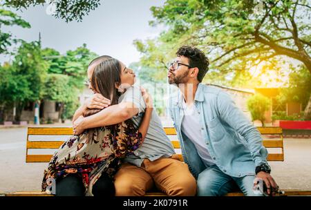 Untreue Frau, die ihren Freund umarmt und heimlich einen anderen Mann küsst. Untreue Freundin umarmte ihren Freund heimlich in einem Park Stockfoto