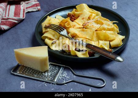 Pappardelle, gekochte, breite italienische Bandnudeln mit Bolognese-Sauce auf dem Teller, geriebener Käse, Pasta, Nudeln Stockfoto