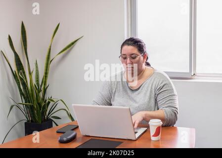 Porträt einer Frau mittleren Alters, die im Büro an ihrem Laptop arbeitet Stockfoto