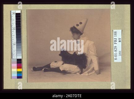 Mädchen in einem pierrot-Kostüm mit einem kleinen schwarzen Hund auf dem Schoß, zwischen 1900 und 1920. Stockfoto