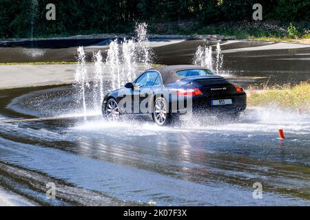 Sportwagen mit Allradantrieb der Porsche 911 Carrera 4s fährt mit 50 km/h Geschwindigkeit auf abschüssiger, stark bewässert nasser Straße auf Hindernis aus dem Wasser zu Stockfoto