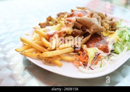 Döner Kebab auf einem Teller mit Pommes frites, Salat und verschiedenen Saucen auf einem Teller, beliebtes Fast Food aus der türkischen Küche, Kopierraum, ausgewählter Fokus, nar Stockfoto