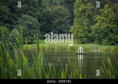 Kleine künstliche Insel mit weißem Pavillon für Wasservögel am See im idyllischen Landschaftspark Putbus mit Schilf am Ufer, großer alter See Stockfoto