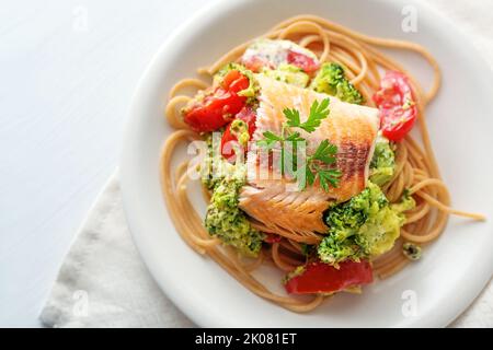 Wildlachsfilet auf Vollkornspaghetti mit Brokkoli, Tomaten und Petersilie garnieren, gesunde Mahlzeit auf weißem Teller, Tempo kopieren, Hochwinkel-Ansicht Stockfoto