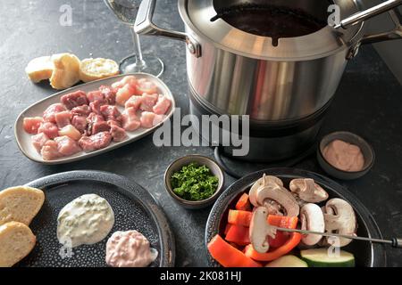 Öl-Fondue mit Fleisch und Gemüse in einem Topf mit heißem Fett gebraten werden, festliches Abendessen oft auf Partys wie Neujahr serviert, ausgewählte Fokus, schmal de Stockfoto