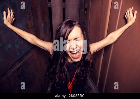 Nahaufnahme Porträt einer jungen Dame in schwarzem Kleid ruht seine Hände gegen die schrumpfenden Wände und schreit verzweifelt in der Nacht auf geschlossenen Raum Stockfoto