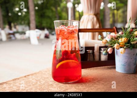Rote Erdbeer-Limonade mit Limonade, Eis, Orangenscheibe und Minzblättern in Glasflasche oder Krug auf dem Tisch. Street Cafe. Vorderansicht. Stockfoto