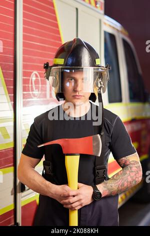 Foto von Feuerwehrmann mit Helm und Axt gegen Feuerwehrmann. Stockfoto