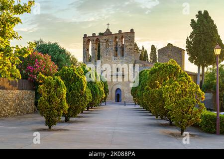 Alte Steinkirche mit Spaziergang mit Bäumen bei Sonnenuntergang in der Stadt Peratallada, Girona, Spanien. Stockfoto