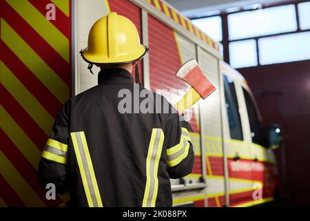 Feuerwehrmann voll ausgestattet mit Helm und Axt im Feuerwehrauto Hintergrund. Stockfoto