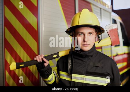 Feuerwehrmann voll ausgestattet mit Helm und Axt im Feuerwehrauto Hintergrund. Stockfoto