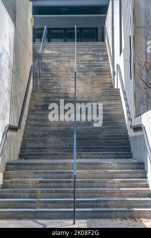 Treppe eines Gebäudes, das zum oberen Stockwerk führt und Eingang mit Glastüren. Blick von unten auf eine Treppe mit Stahlgeländern und Betonstufen Stockfoto