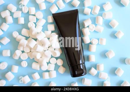Mockup schwarz Squeeze Flasche kosmetischen Rohr und weißen Mini-Marschmallows viel auf blauem Hintergrund. Creme, Gleitgel, Feuchtigkeitscreme, Hautpflege, Sonnencreme Stockfoto