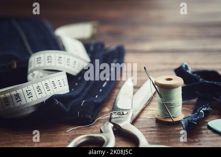 Verkürzende Jeans. Maßband, Schere, Garnspulen und Kreide auf Holztisch. Jeans-Schnitt. Stockfoto