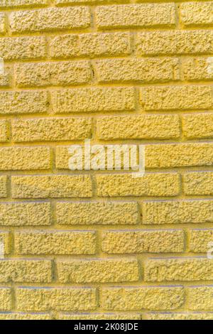Nahaufnahme einer Gebäudeaußenwand mit rauer Struktur und gelber Farbe. Nahaufnahme einer staubigen strukturierten Ziegeloberfläche mit geometrischem Muster Stockfoto