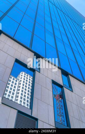 Modernes Gebäude außen mit Glasfassade, die einen Baukran widerspiegelt. Die Fenster spiegeln auch Wohnungen oder Büros und den blauen Himmel im Himmel wider Stockfoto