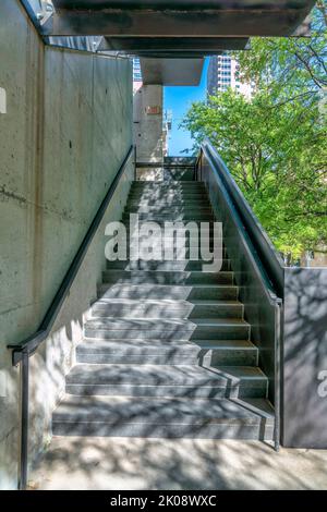 Blick vom unteren Ende der Treppe, die zu einem Gebäude in Austin Texas führt. Außentreppe mit sonnenbeschienenen Betonstufen und Metallgeländern dagegen Stockfoto
