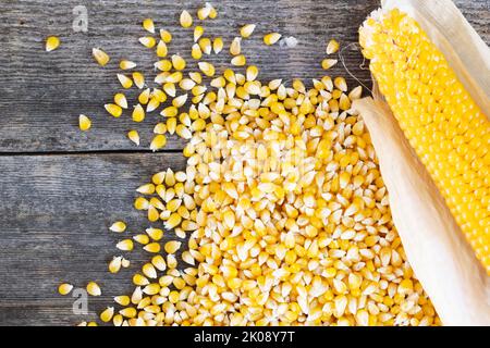 Popcorn auf dem Cob und Kerne auf einem rustikalen Holztisch aus und über dem Kopf gesehen Stockfoto