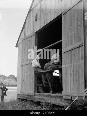 Wright Flights, Fort Myer, Virginia, Juli 1909 - First Army Flights; Hangar, Wilbur Wright, Rechts, Zeigt Seinen Einwand, Fotografiert Zu Werden. [Die Gebrüder Wright führten Testflüge in Fort Myer durch, nachdem ihnen das US-Kriegsministerium einen Vertrag von $25.000 angeboten hatte, wenn ihr Flyer eine Geschwindigkeit von 40 Meilen pro Stunde erreichte]. Stockfoto