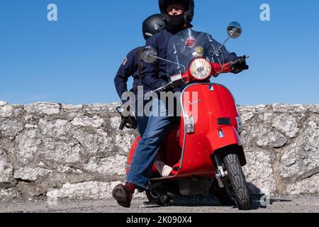 Vintage Vespa Scooter, der bei der Rollerrallye rot, Fahrer und Sozius auffällt. Ballintoy, Großbritannien - 10. September 2022. Stockfoto