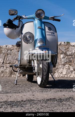 Zweifarbiger Li-Roller in Blau und weiß, geparkt mit weißem Crashhelm am Lenker. Ballintoy, Großbritannien - 10. September 2022. Stockfoto