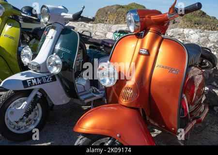 Drei klassische italienische Lambretta-Motorroller entlang der Meeresmauer am Hafen, Treffen der Clans-Rallye. Ballintoy, Großbritannien - 10. September 2022. Stockfoto