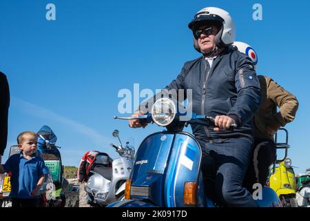 Mann auf blauem Vespa-Roller mit Beifahrer beim jährlichen Treffen der Clans-Roller-Rallye. Ballintoy, Großbritannien - 10. September 2022. Stockfoto