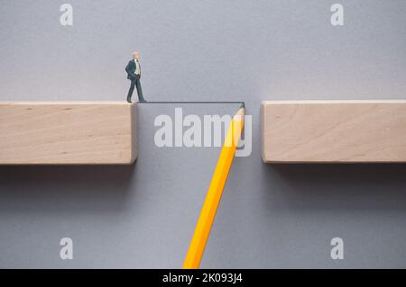 Miniatur-Geschäftsmann, der eine Linie überquert, die mit einem Bleistift skizziert wurde und die Lücke zwischen Holzblöcken überbrückt Stockfoto