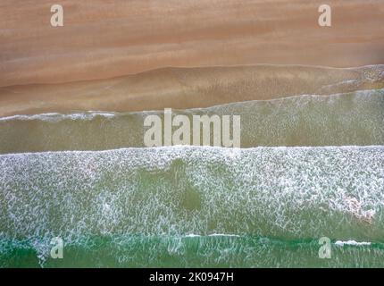 Drone-Ansicht von oben auf das türkisfarbene Meer und die weiß getünchte Wellen, die an einem leeren goldenen Sandstrand brechen Stockfoto