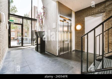 Glänzender Aufzug mit geöffneter Tür in der beleuchteten Halle eines modernen Apartmentgebäudes mit Fliesenboden Stockfoto