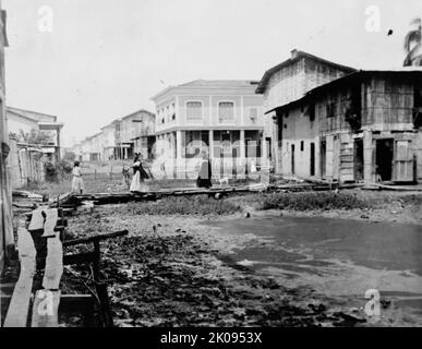 Ecuador - Szenen in Quayaquil [sic], Ecuador, 1912. „Straßenszene am Rande des besseren Teils der Stadt“. Frauen gehen auf einem erhöhten Holzsteg über Schlamm. Stockfoto