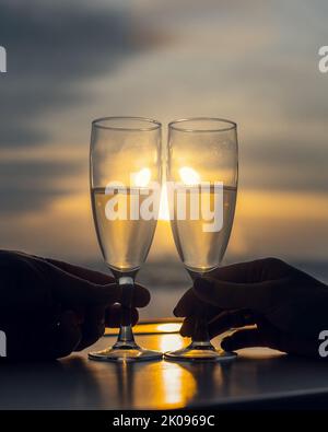 Zwei Gläser mit Champagner klinken Gläser vor dem Hintergrund des Fensters bei Sonnenuntergang Stockfoto