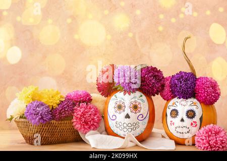 Kürbisse mit bemalten Schädeln und Blumen auf farbigem Hintergrund. Feier von Halloween oder Mexikos Tag der Toten Stockfoto