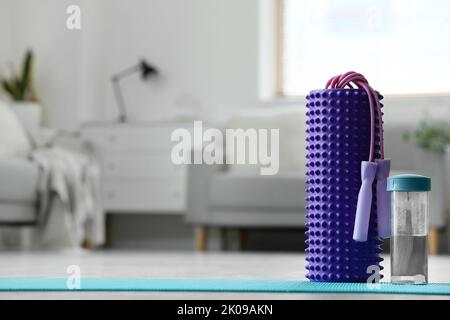 Schaumstoffrolle mit Springseil und Wasserflasche auf Matte im Wohnzimmer Stockfoto