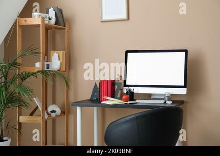 Moderner Arbeitsplatz mit Computer, Buchhalter, Apfel- und Stifttasse in der Nähe einer beigefarbenen Wand im Zimmer Stockfoto