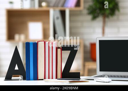 Stilvoller Halter mit Büchern und Laptop auf dem Tisch im Zimmer Stockfoto