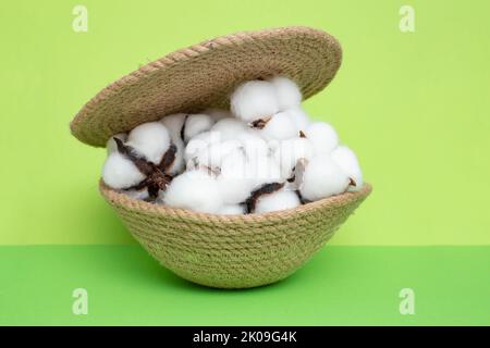 Korb aus Jute-Seil mit Deckel, voller Baumwollblumen, auf grünem Hintergrund. Nahaufnahme der Seitenansicht Stockfoto