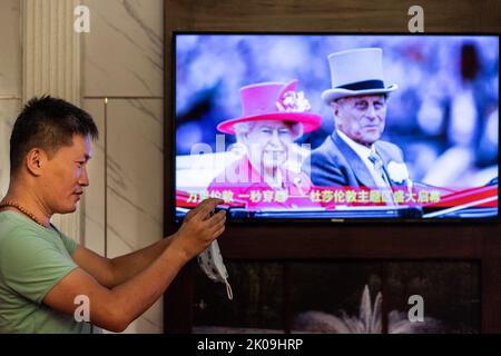 Ein Mann fotografiert neben Fotos vom Besuch der britischen Königin Elizabeth II. In China bei Madame Tussauds. Königin Elizabeth II., die dienstälteste Monarchin der britischen Geschichte und eine Ikone, die Milliarden von Menschen auf der ganzen Welt sofort zu erkennen ist, starb am 8. September im Alter von 96 Jahren auf ihrem schottischen Hochland-Retreat. Stockfoto