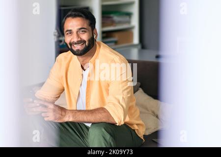 Glücklicher indischer Mann, der zu Hause auf der Couch mit Telefonmusik sitzt. Stockfoto